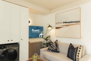 Un saló amb un sofà, una televisió que mostra la marca 'fluent', un radiador i un quadre amb un paisatge emmarcat.