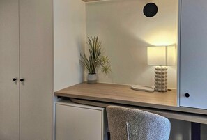 Una habitación con un escritorio, una planta en maceta, una lámpara y una silla.
