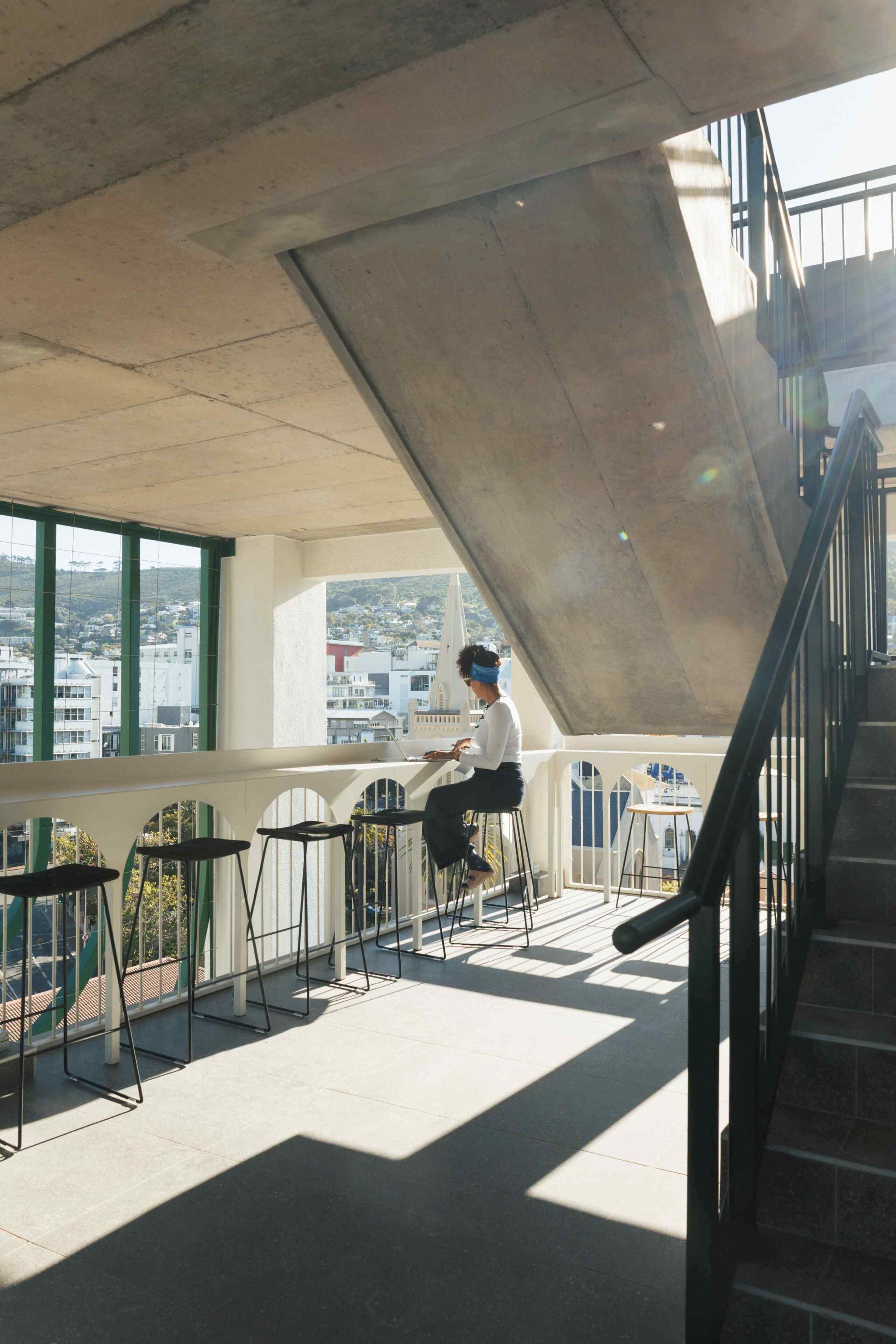 A person sitting on a balcony with a city view, a staircase, and a railing.