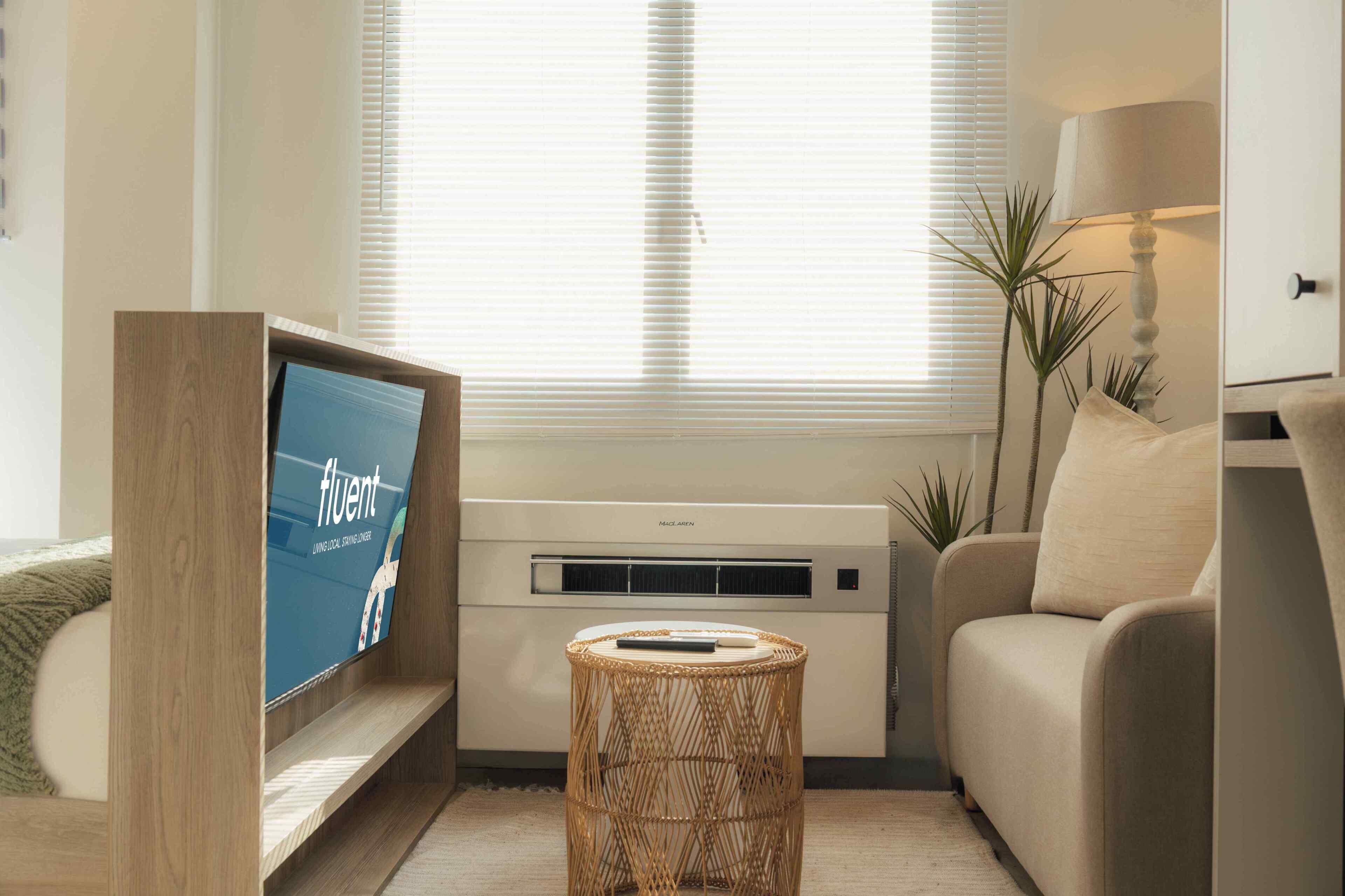 Una sala de estar moderna con televisor, aire acondicionado instalado en la pared, una mesa de centro de mimbre, un sofá y una lámpara.