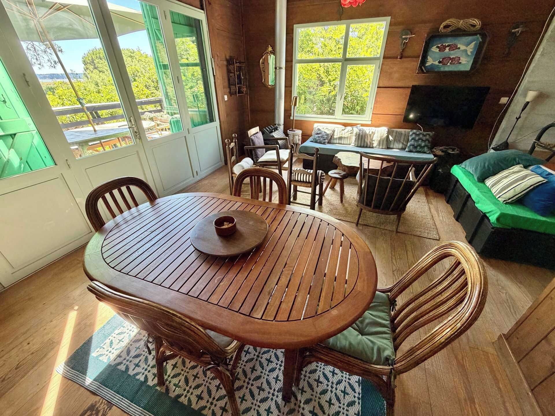 A wooden dining table with chairs, a sofa, and a television in a room with large windows.