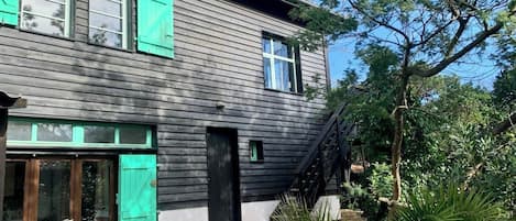 Et toetagers hus med mørk facade, grønne skodder og en lille veranda.