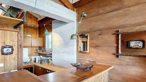 Interior de fusta amb zona de cuina, incloent-hi armaris, un rentapeus i una taulell.