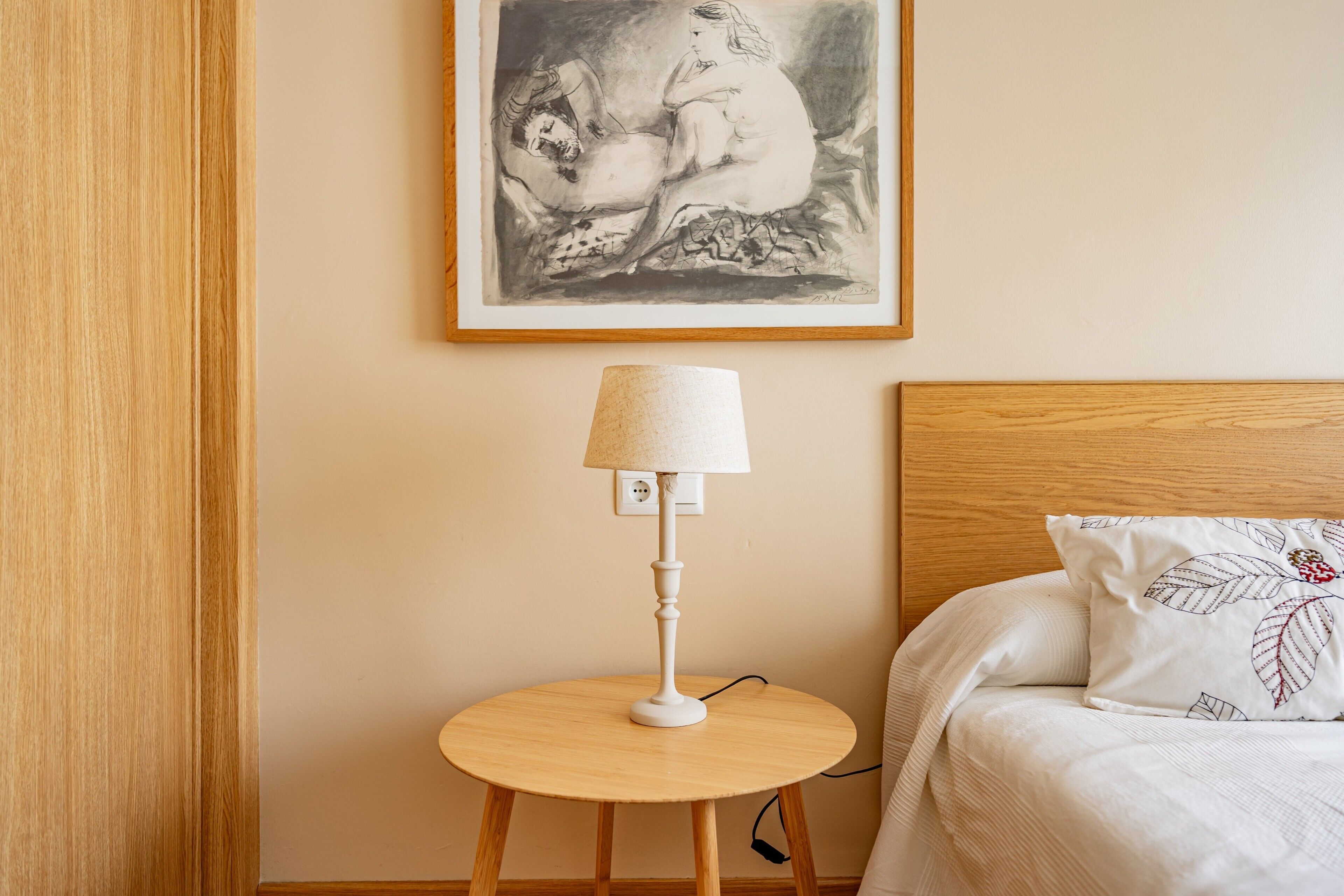 Une chambre à coucher avec un lit, une table de chevet avec une lampe et une œuvre d’art encadrée accrochée au mur.