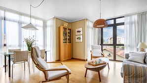 A modern living room with a sofa, armchair, dining table, and a large window with a view. - Isla de Cuba 2K Apartment – Colombres (Colombres)
