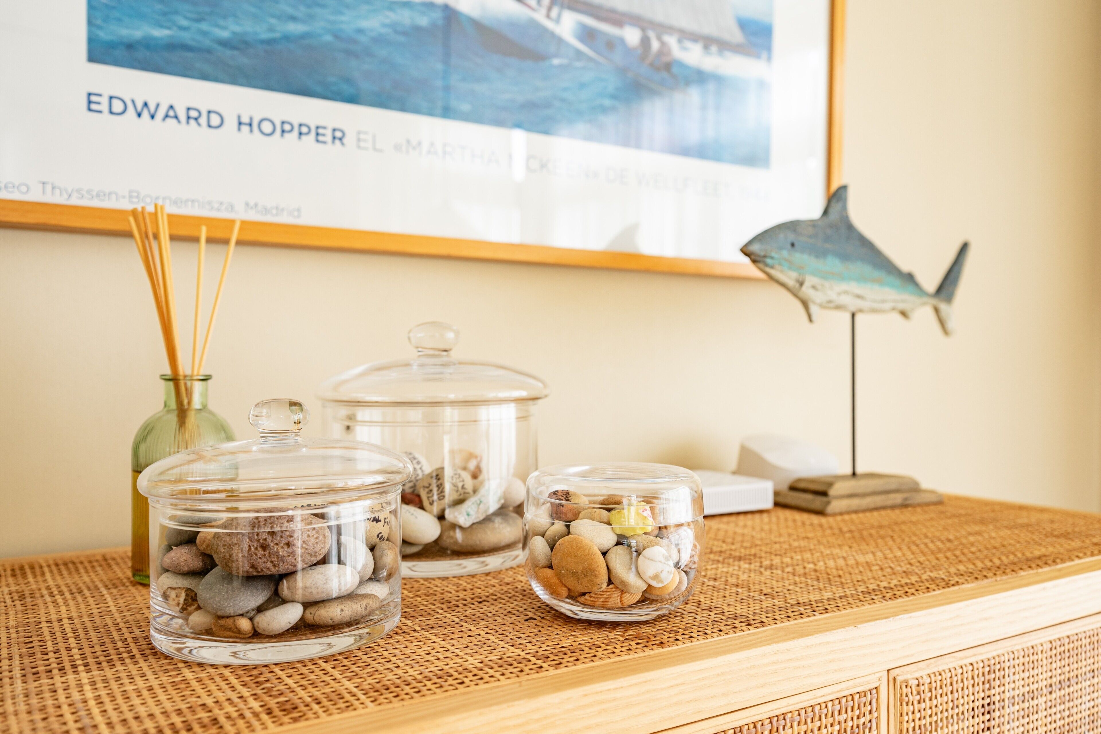 Three glass jars with stones on a woven surface, a framed picture, and a shark decoration.
