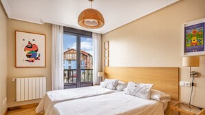 A hotel room with two beds, a wooden headboard, a radiator, a window with a view of buildings, and a poster on the wall. - Isla de Cuba 2K Apartment – Colombres (Colombres)