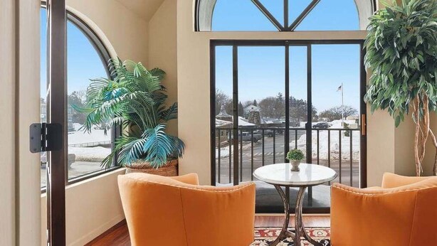 A room with two orange chairs, a small table, and a view of a parking area through a large window. - 391 Edgewater | Downtown Charlevoix | Pool, Hot Tub, Sauna | Full Kitchen (Charlevoix)