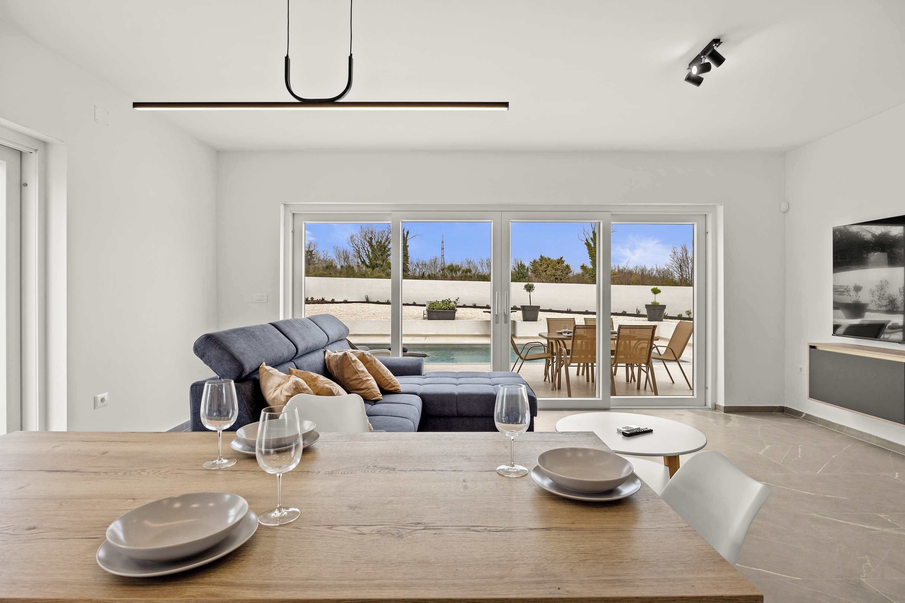 Een moderne woonkamer met een eettafel, bank en uitzicht op een zwembad en terras.