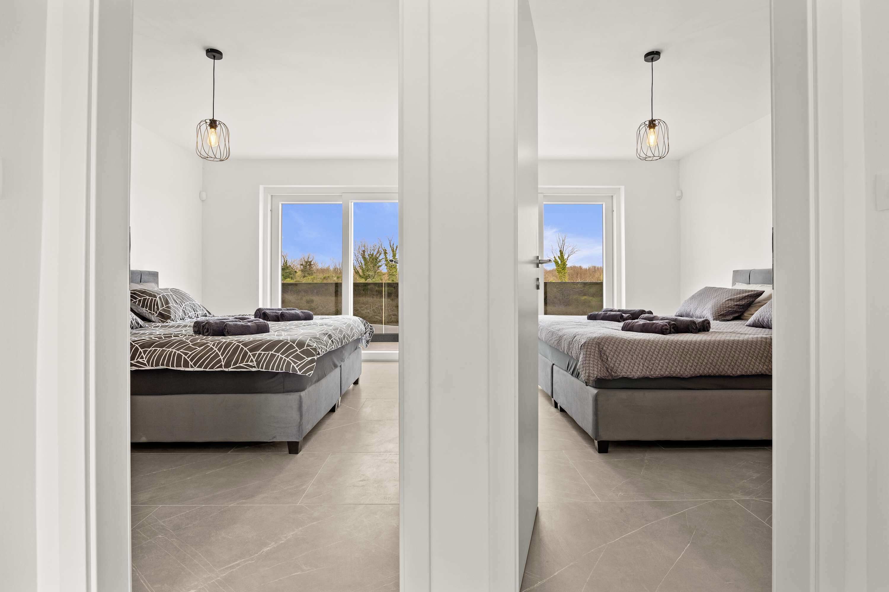 Une chambre moderne avec deux lits, de grandes fenêtres et une vue sur l’extérieur.