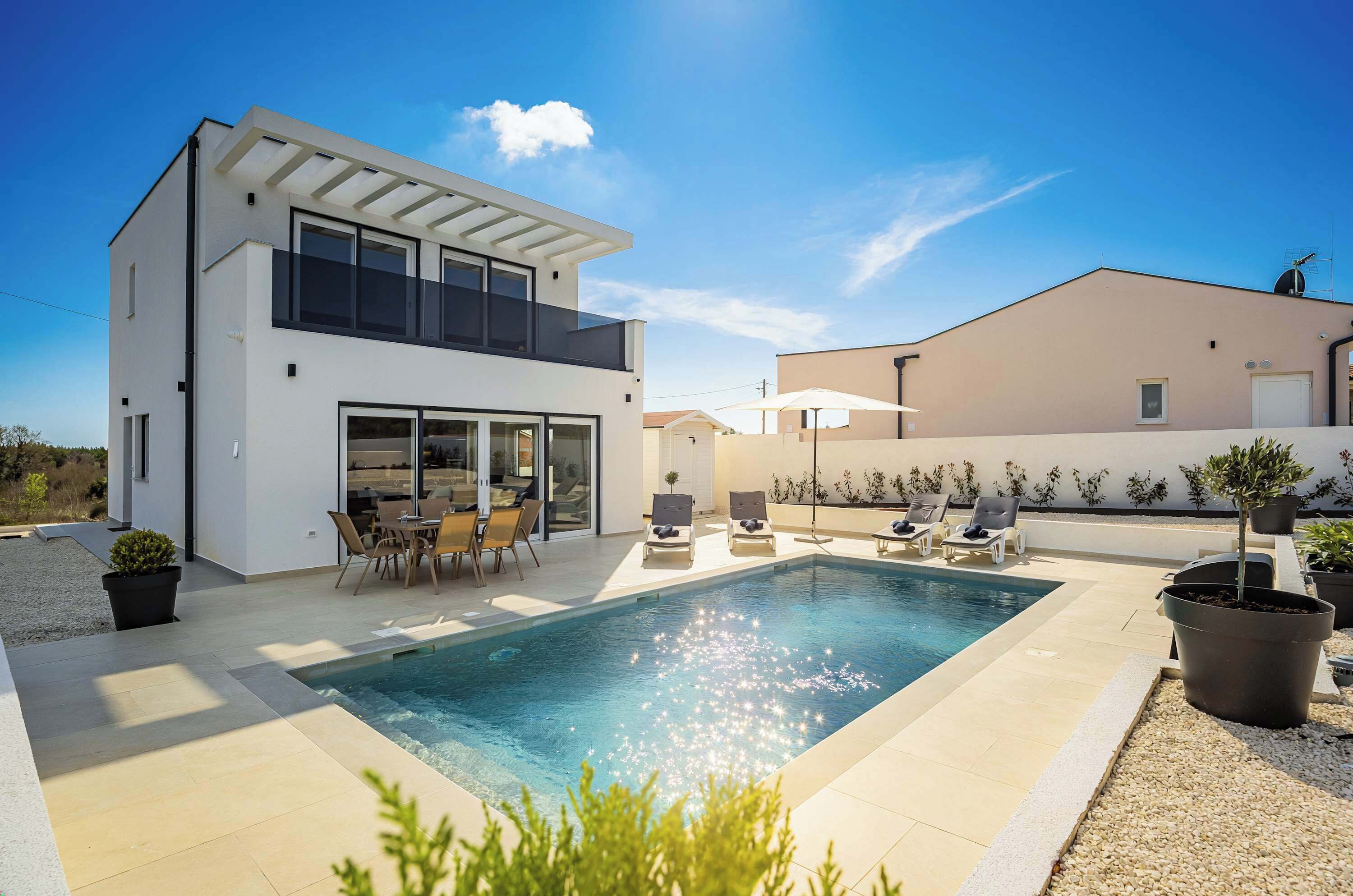 A modern two-story house with a swimming pool, outdoor seating, and a pergola.