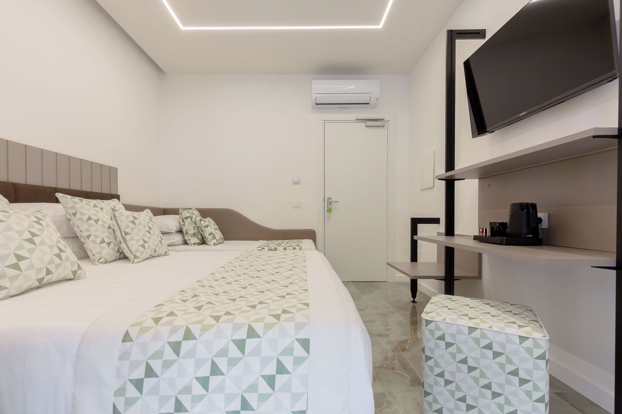 Una habitación de hotel moderna con una cama, un televisor, una cafetera y un equipo de aire acondicionado.