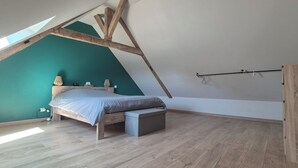 A bedroom with a sloped ceiling, a bed, a bench, a wardrobe, and a skylight. - Country house (Vivoin)