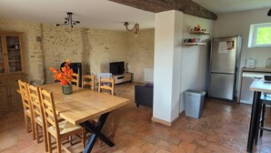 A rustic kitchen with a wooden dining table, chairs, a TV, and a refrigerator. - Country house (Vivoin)