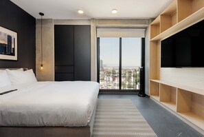 Een moderne hotelkamer met een groot bed, een flatscreen televisie, een balkon met uitzicht op de stad en ingebouwde planken.