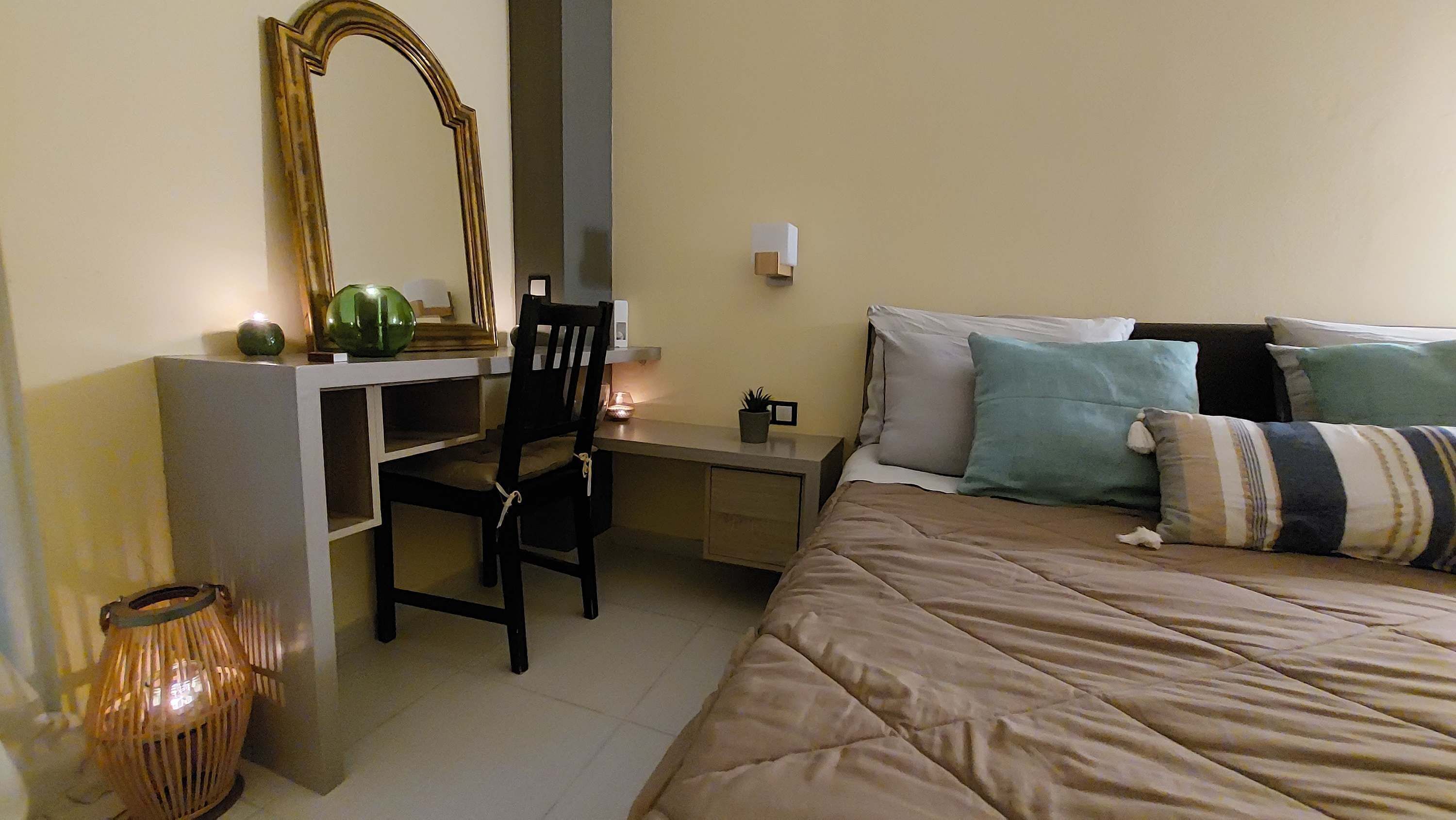 Een slaapkamer met een bed, een bureau, een stoel, een spiegel en een nachtkastje.