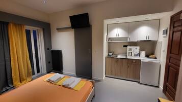 A bedroom with a bed, a small kitchenette, and a TV mounted on the wall.