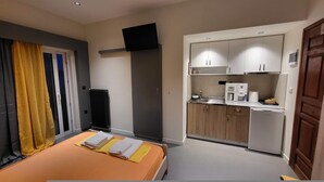A compact hotel room with a bed, a small kitchenette, and a TV mounted on the wall. - Tsiamis Sea Sun - Quaint and Homely Getaway (Corinth)