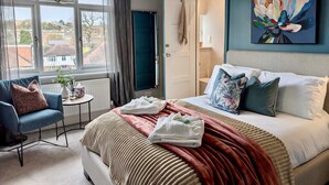 A hotel room with a bed, a chair, a small table, a window with curtains, and a painting on the wall. - 2 Private Ensuite Rooms Shared With Friendly Host (London)