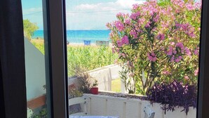 Um pátio com mesa e cadeiras, vista para o mar e um arbusto de flores cor-de-rosa.