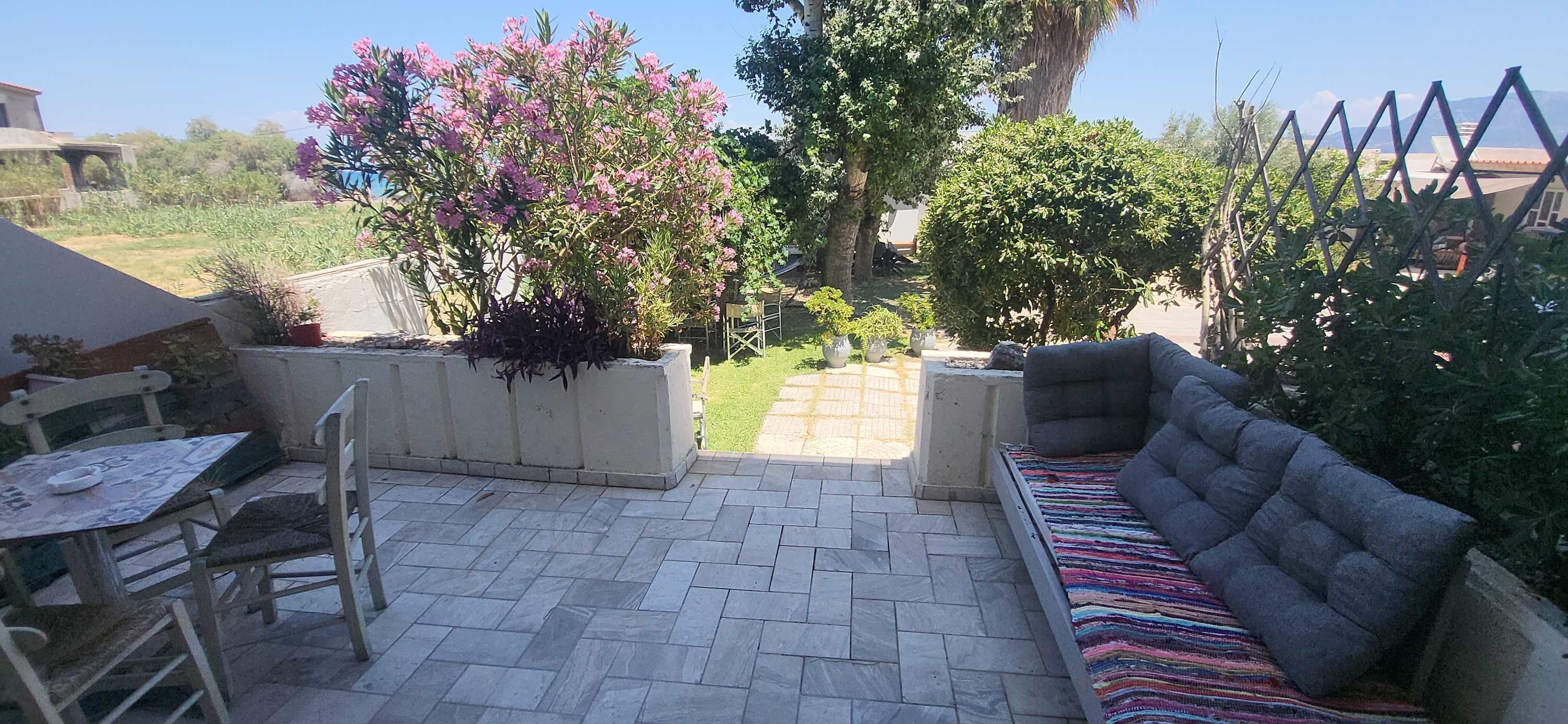 Un patio con un sofá, una mesa y sillas. Hay plantas en macetas y se ve un jardín.