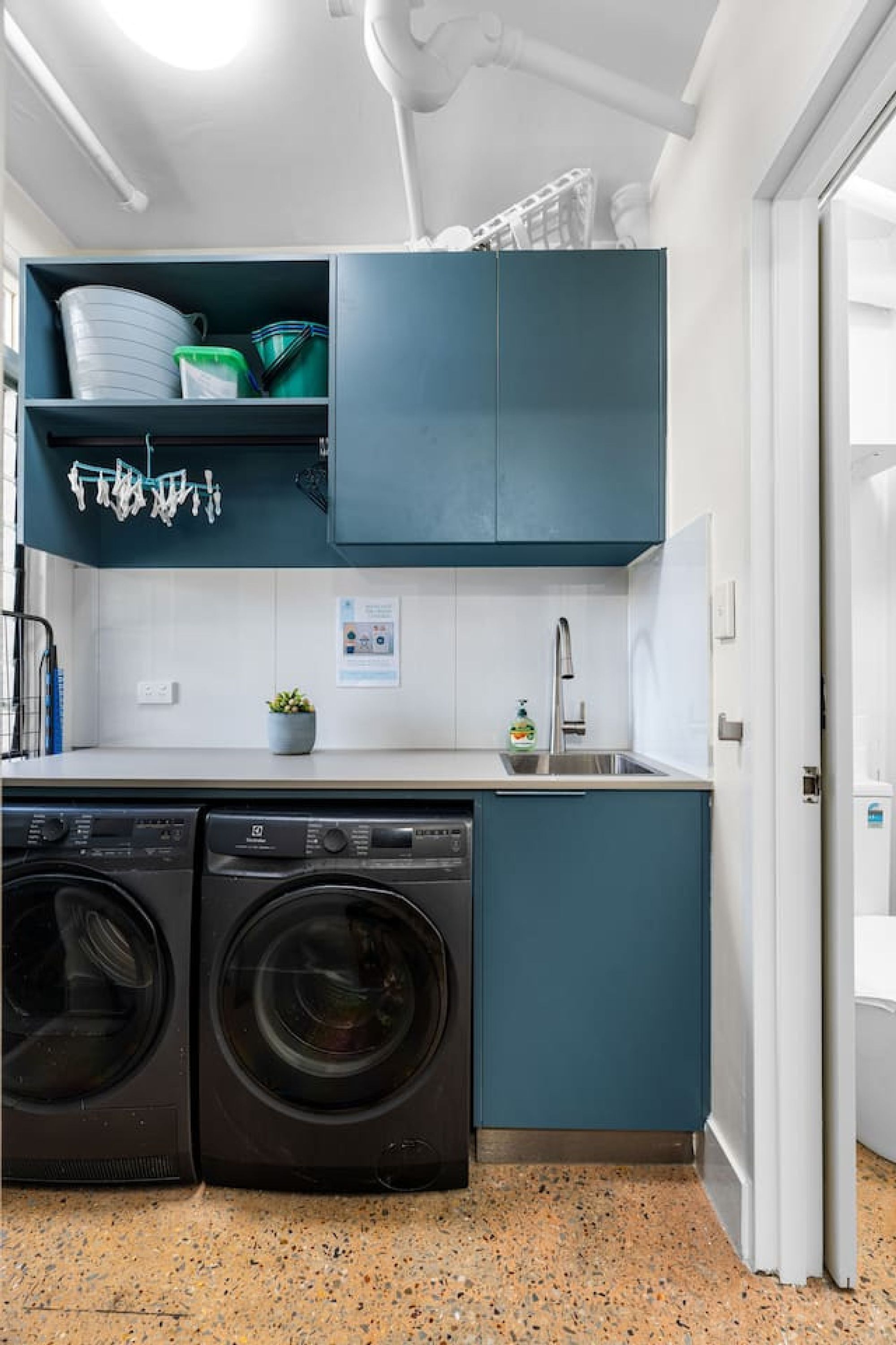 Une cuisine de taille réduite, équipée d’un lave-linge, d’un évier et de meubles de couleur turquoise.