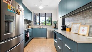 Une cuisine moderne dotée d’appareils électroménagers en acier inoxydable, de meubles de couleur turquoise et d’une fenêtre offrant une vue sur la verdure.
