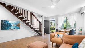 Un salon moderne avec un escalier, un coin repas et une grande fenêtre avec des rideaux.