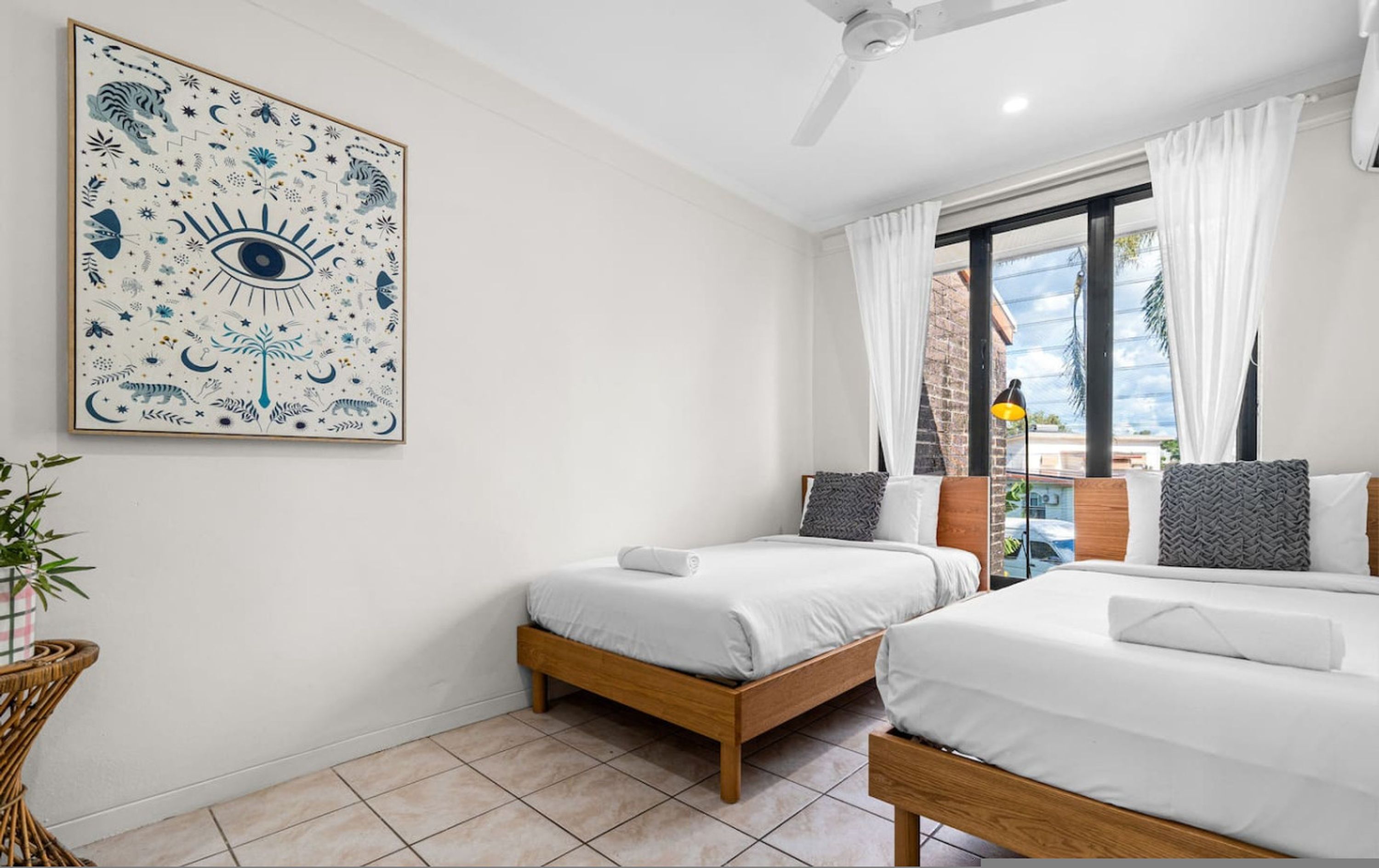 A hotel room with two beds, a large wall art, a window with curtains, and a view of the outside.