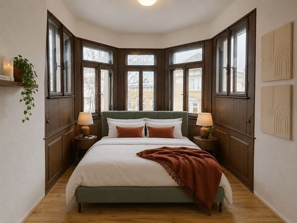 Un dormitorio con una cama grande, dos mesitas de noche, un cabecero verde y varias ventanas.