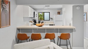 Una cocina moderna con armarios blancos, una isla central con sillas, un ventilador de techo y vistas al exterior.