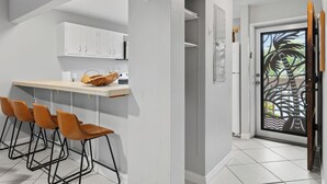 Una cocina con armarios blancos, una barra con taburetes y una puerta decorada con diseño de palmera.