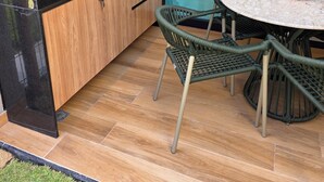 Une cuisine moderne équipée d’un évier, d’un plan de travail et de meubles en bois. On y trouve une table ronde avec des chaises, et une porte vitrée donne sur un espace extérieur.