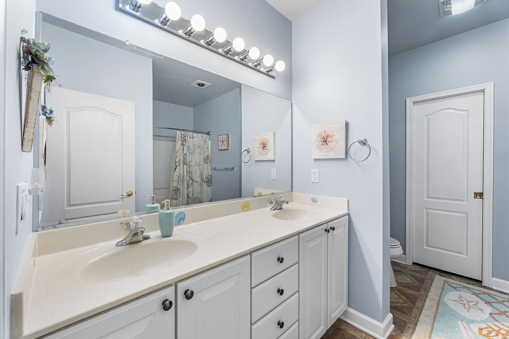 Une salle de bain avec un double lavabo, un grand miroir et un rideau de douche.