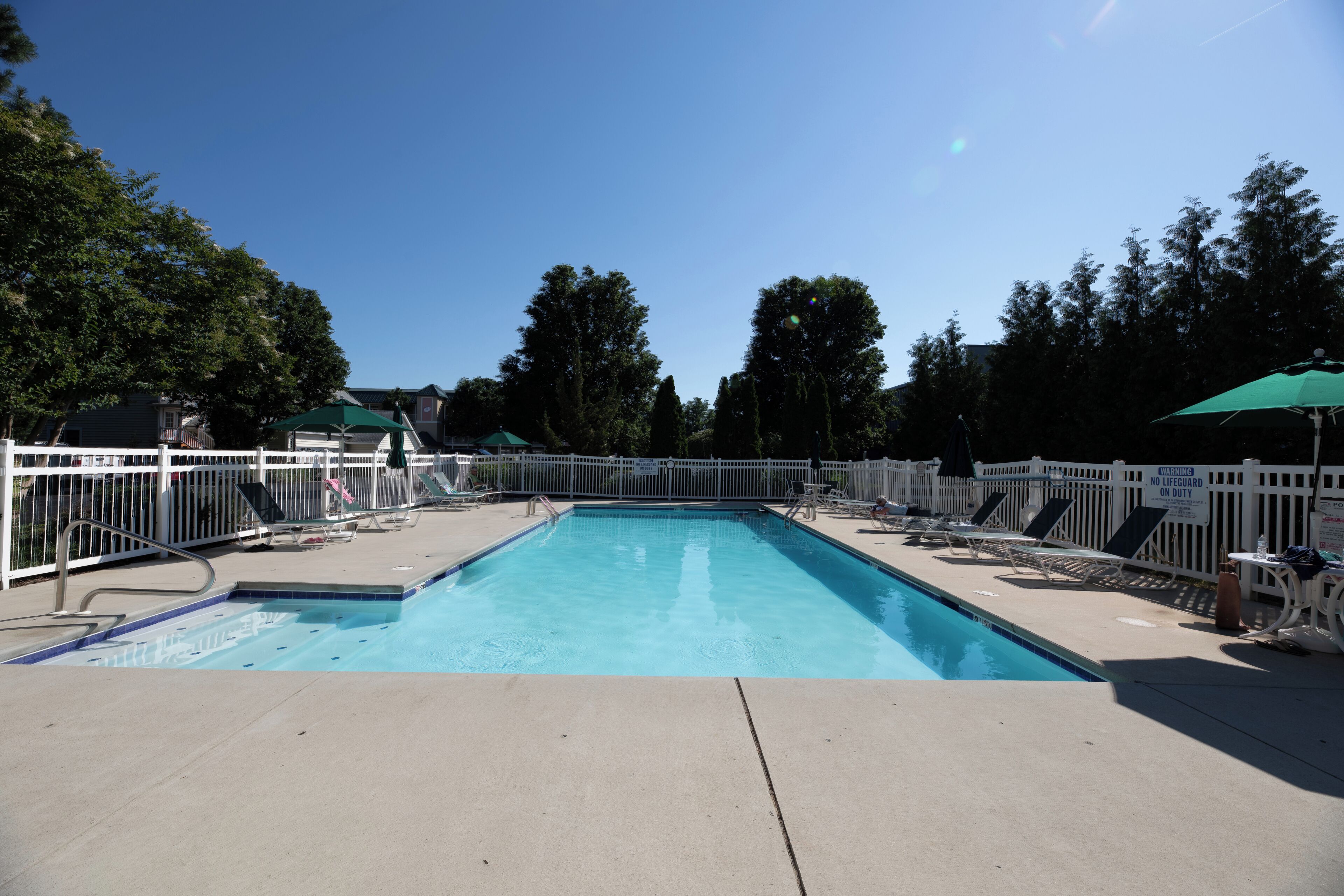 A rectangular swimming pool with a white fence, lounge chairs, and umbrellas.