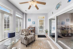 Un salon avec un ventilateur de plafond, un fauteuil à rayures, une table en verre et un tapis à motifs.