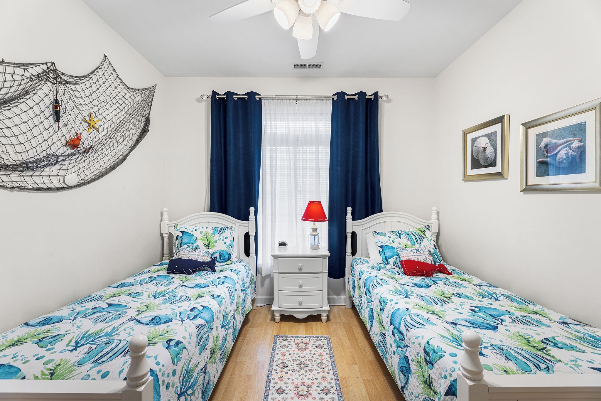 A bedroom with two beds, a nightstand, a red lamp, and a decorative net on the wall.