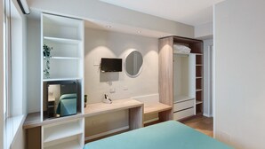 Une chambre à coucher moderne, équipée d’un lit, d’un bureau, d’une télévision, d’un miroir et d’étagères intégrées.