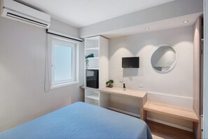 Ein Schlafzimmer mit Bett, Fernseher, Spiegel, Fenster und einer integrierten Küchenzeile.