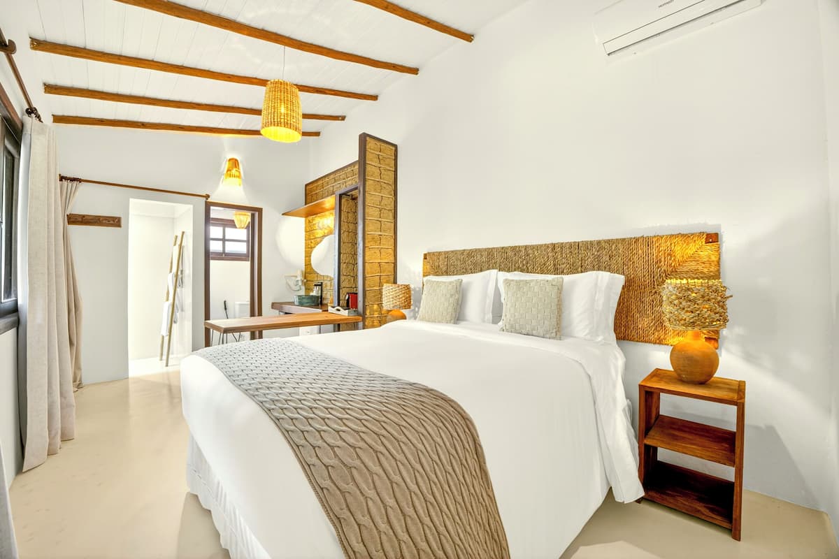 A bedroom with a large bed, a wooden headboard, a bedside table with a lamp, and a mirror.