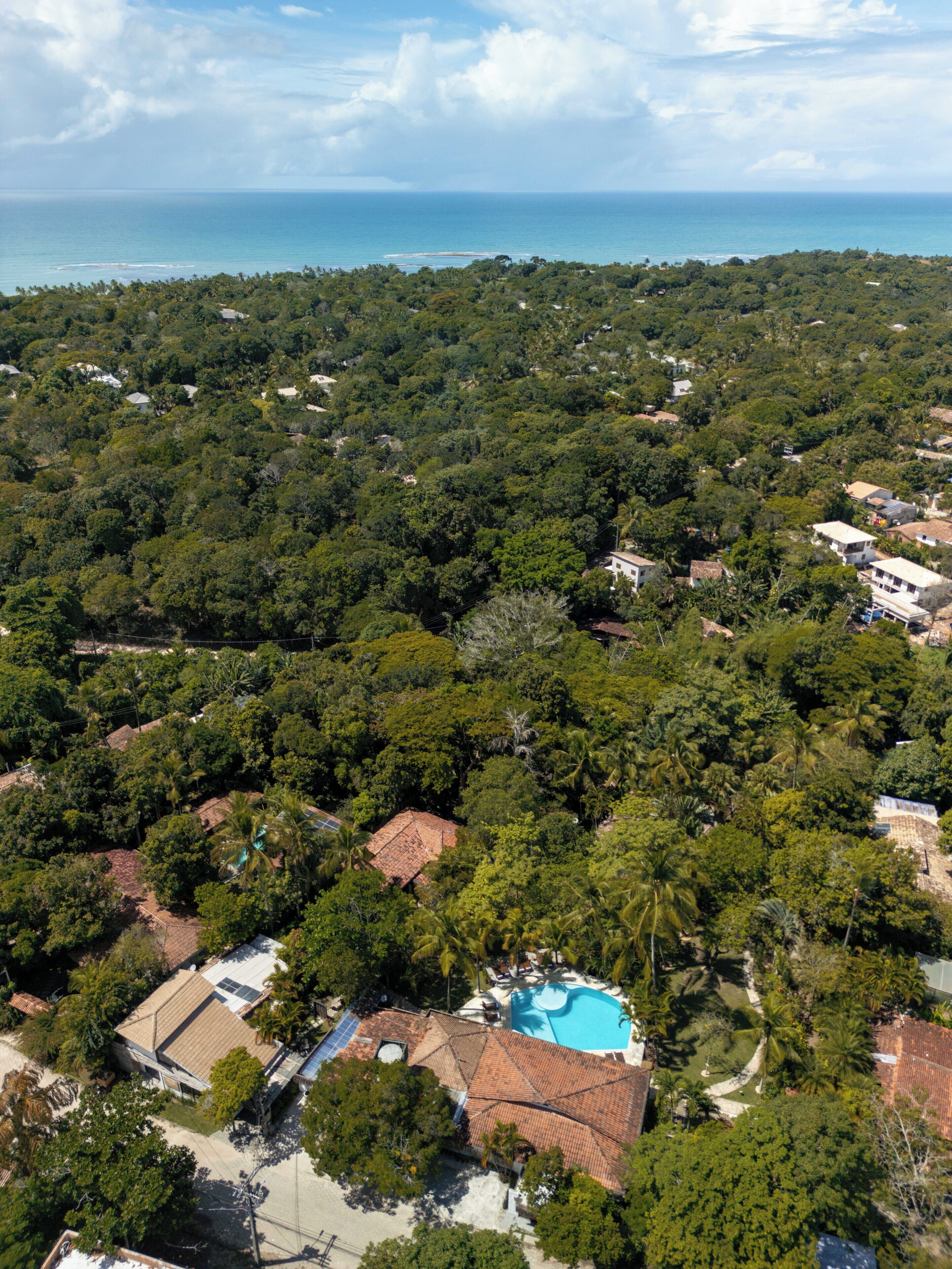 An aerial view of a residential area with a swimming pool surrounded by lush greenery and houses with red-tiled roofs.