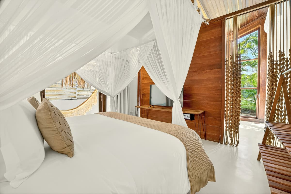 A bedroom with a bed, a TV, and a view of greenery.