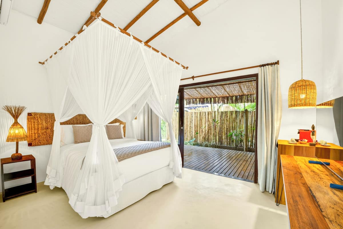A bedroom with a canopy bed, a wooden desk, and a view of the outdoors.