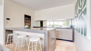 Une cuisine moderne dotée d’un îlot central, de tabourets de bar, d’un four encastré et d’une grande fenêtre.