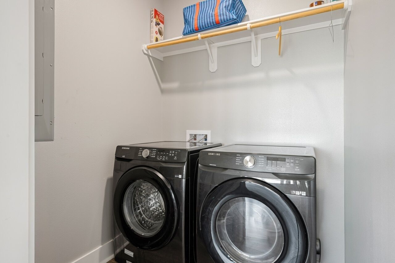 Two front-loading washing machines in a laundry room with a shelf above holding a bag and a box.