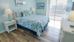 A bedroom with a bed, two wall-mounted lamps, a ceiling fan, and a large window with a view of buildings. - 1815 North Hampton, Ocean View Condo With Full Access!! 3 Bedroom Condo (Myrtle Beach)