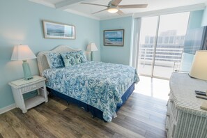 A bedroom with a bed, two wall-mounted lamps, a ceiling fan, and a large window with a view of buildings. - 1815 North Hampton, Ocean View Condo With Full Access!! 3 Bedroom Condo (Myrtle Beach)