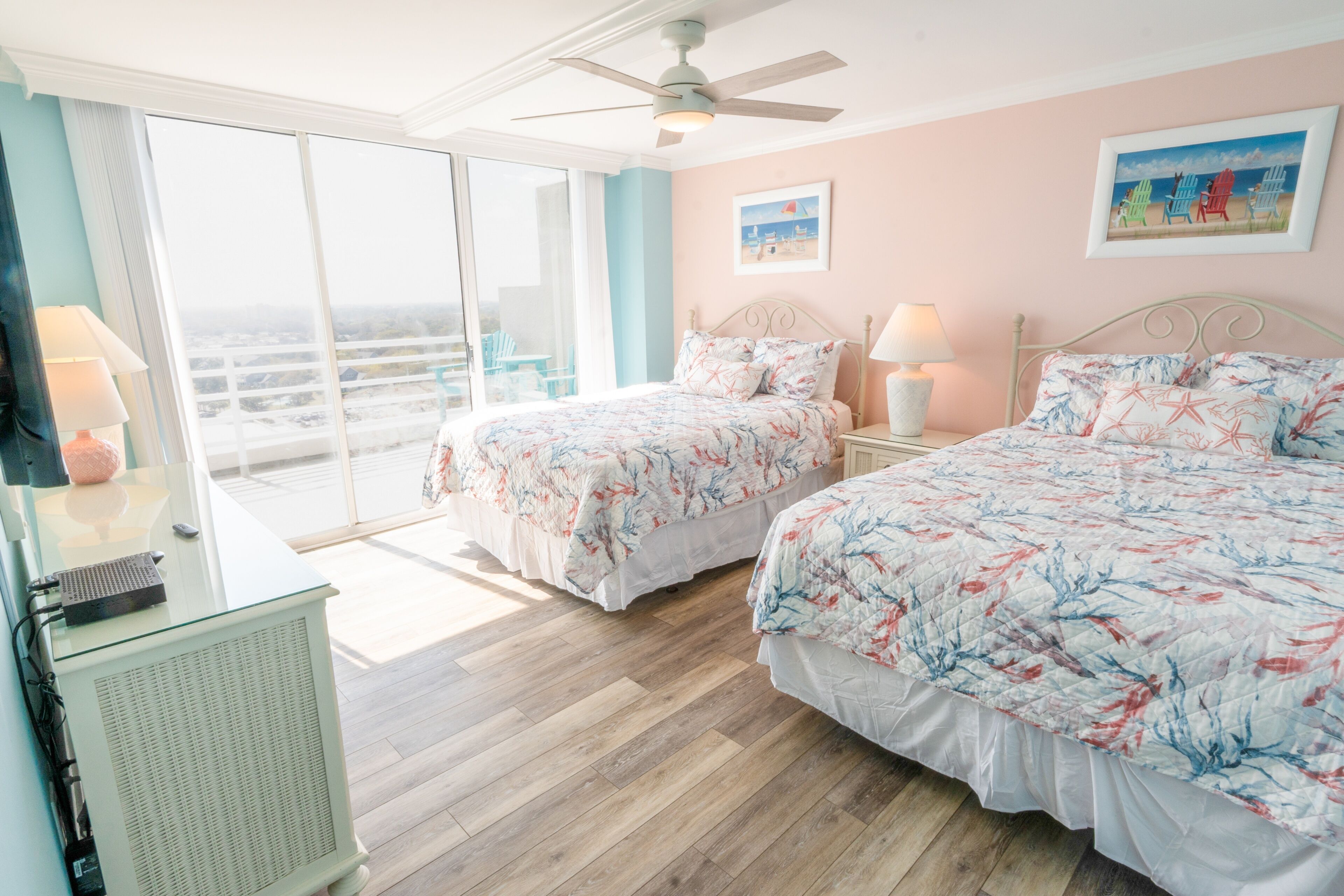 A bedroom with two beds, a ceiling fan, and a view through a sliding glass door.
