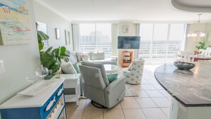 A modern living room with a sofa, a coffee table, a TV, and a balcony with a view. - 1815 North Hampton, Ocean View Condo With Full Access!! 3 Bedroom Condo (Myrtle Beach)