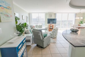 A modern living room with a sofa, a coffee table, a TV, and a balcony with a view. - 1815 North Hampton, Ocean View Condo With Full Access!! 3 Bedroom Condo (Myrtle Beach)
